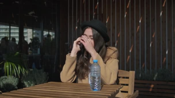 Linda adolescente está respondiendo en la llamada móvil en la terraza abierta de la cafetería
 - Metraje, vídeo