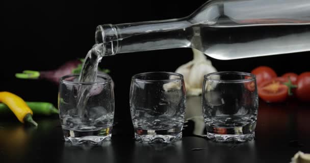 Versi la vodka di alcool da una bottiglia in tre bicchierini. Sfondo con verdure
 - Filmati, video