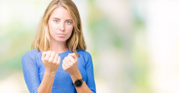 Beautiful young woman wearing blue sweater over isolated background Ready to fight with fist defense gesture, angry and upset face, afraid of problem - Photo, Image