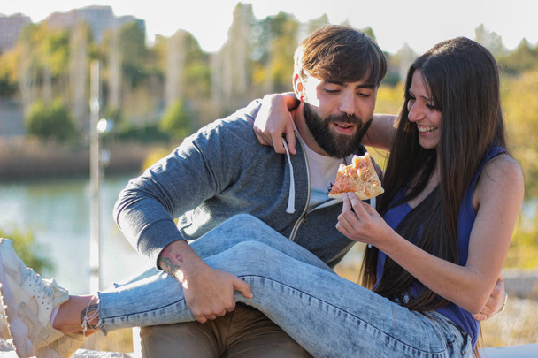 Pareja comiendo pizza al aire libre y sonriendo.Están compartiendo pizza
 - Foto, imagen