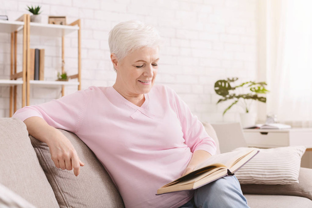 Усміхнена старша жінка читає книгу вдома
 - Фото, зображення