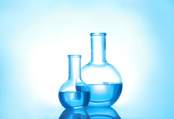 Laboratory glassware with liquid on color background. Solution chemistry - Фото, изображение