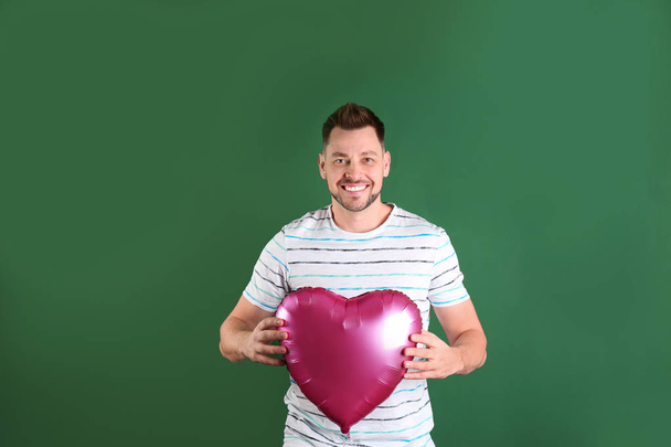Portrait of young man with heart shaped balloon on color background - Photo, Image