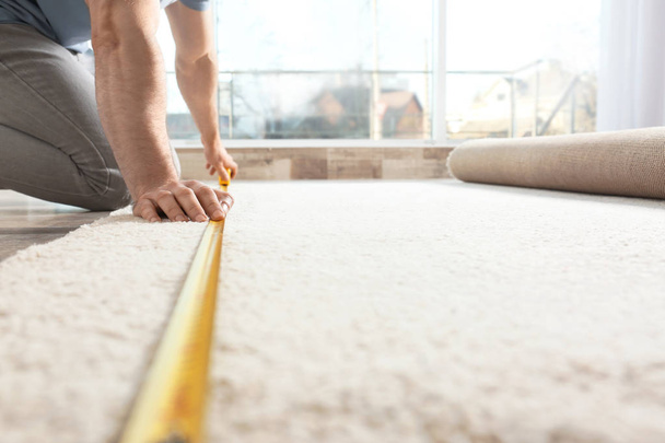 Man measuring carpet indoors. Construction tool - Foto, Imagen