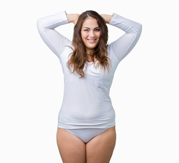 Beautiful plus size young overwight woman wearing white underwear over isolated background Relaxing and stretching with arms and hands behind head and neck, smiling happy - Photo, Image