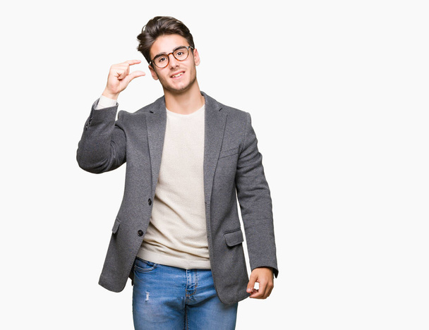 Joven hombre de negocios con gafas sobre fondo aislado sonriente y seguro gesto con la mano haciendo signo de tamaño con los dedos mientras mira y la cámara. Concepto de medición
. - Foto, Imagen