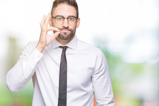 Young handsome business man wearing glasses over isolated background mouth and lips shut as zip with fingers. Secret and silent, taboo talking - Фото, изображение