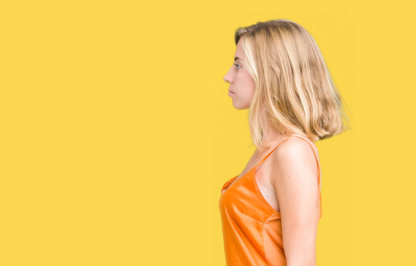 Mooie jonge vrouw die het dragen van oranje shirt over geïsoleerde achtergrond op zoek naar kant, ontspannen profiel pose met natuurlijke gezicht met vertrouwen glimlach. - Foto, afbeelding