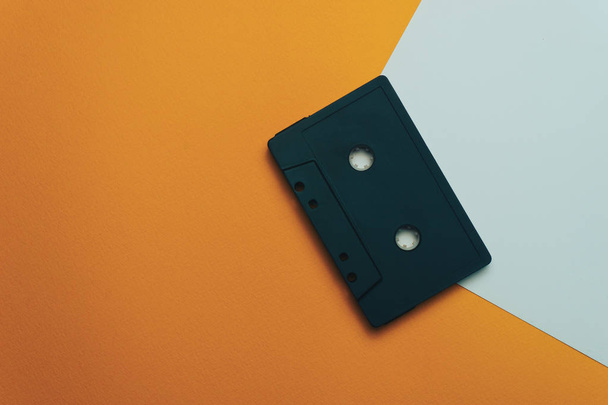 オレンジ色の背景に黒の古典的な磁気カセットテープ. - 写真・画像