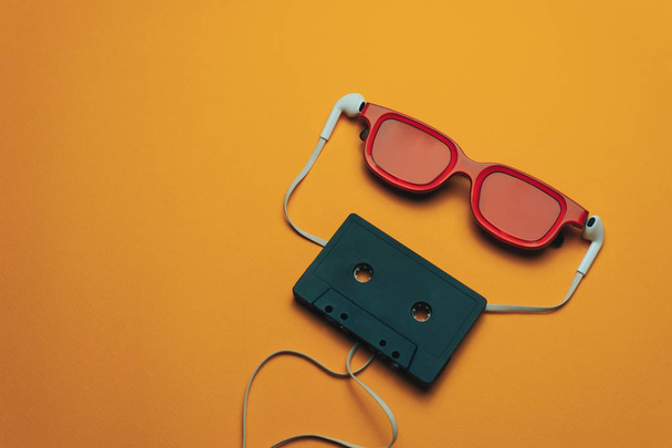 Red glassed, black magnetic cassette tape and  white headphones on a orange background. - Φωτογραφία, εικόνα
