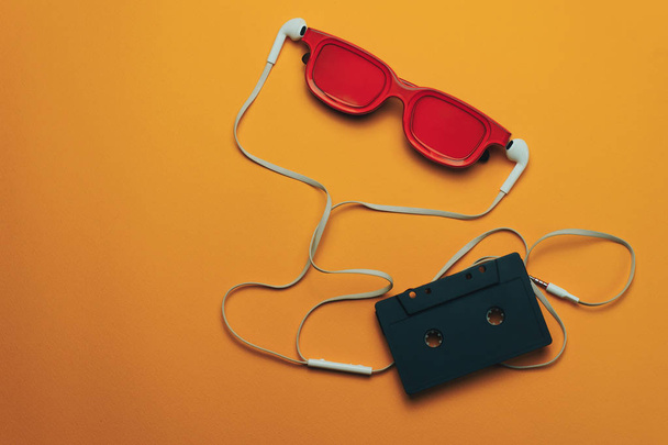 Red glassed, black magnetic cassette tape and  white headphones on a orange background. - 写真・画像