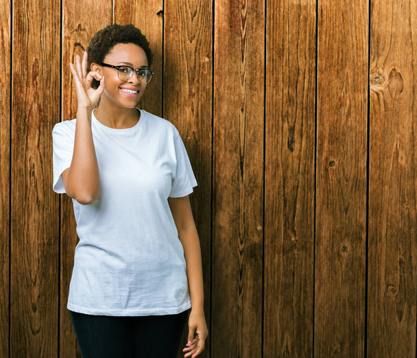 美しい若いアフリカ系アメリカ人女性の孤立した背景を浮かべて手と指で ok サインをしている肯定的な上メガネを着用します。成功した式. - 写真・画像