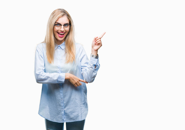 Mladá krásná blondýna obchodní žena nosí brýle izolované pozadí s velkým úsměvem na tváři, rukou a prstu přejdete na straně při pohledu na fotoaparát. - Fotografie, Obrázek