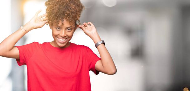 Красивая молодая африканская американка на изолированном фоне, улыбающаяся, дергая за уши пальцами, смешной жест. Задача прослушивания
 - Фото, изображение