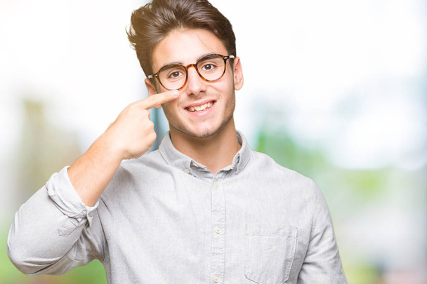 Mladý pohledný muž nosí brýle nad izolované pozadí ukázání prstem ruky do obličeje a nosu, s úsměvem veselá - Fotografie, Obrázek