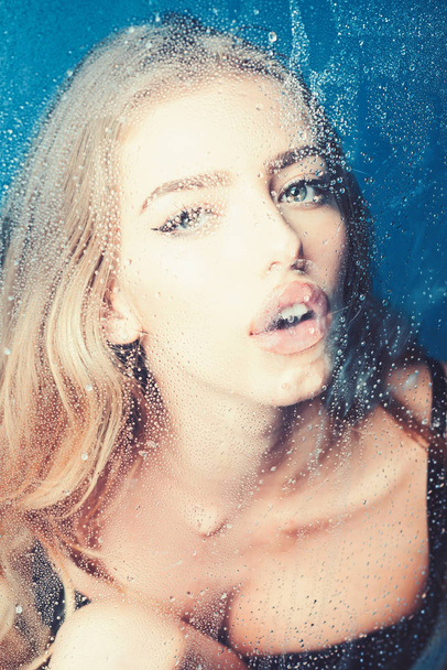 Rain drops on window glass with face of girl. Fashion and beauty. Window with water drops before girl with makeup. Sexy woman behind plastic sheet with water drops. Shower and hygiene spa treatment - Photo, Image