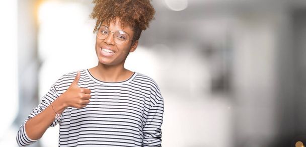 schöne junge afrikanisch-amerikanische Frau mit Brille über isoliertem Hintergrund macht glückliche Daumen nach oben Geste mit der Hand. Zustimmender Blick in die Kamera zeigt Erfolg. - Foto, Bild
