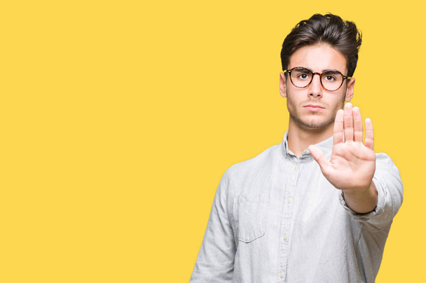 Jonge knappe man dragen bril over geïsoleerde achtergrond stop zingen met de palm van de hand doen. Waarschuwing expressie met negatieve en ernstige gebaar op het gezicht. - Foto, afbeelding