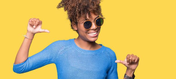Piękna młoda kobieta african american noszenie okularów przeciwsłonecznych na białym tle patrząc pewny siebie z uśmiechem na twarzy, wskazując siebie palcami, dumny i szczęśliwy. - Zdjęcie, obraz