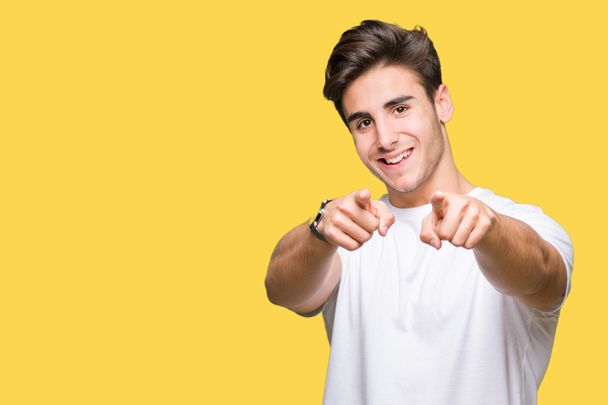 Jonge knappe man dragen witte t-shirt over geïsoleerde achtergrond Pointing aan u en de camera met de vingers, positief en vrolijk lachend - Foto, afbeelding