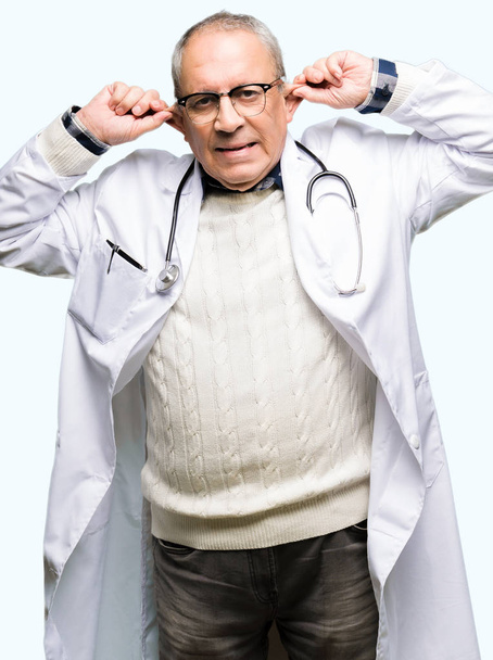 Charmant médecin en manteau médical souriant tirant les oreilles avec les doigts, geste drôle. Problème d'audition
 - Photo, image