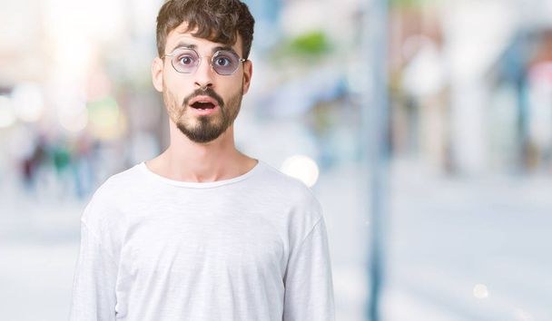 Young handsome man wearing sunglasses over isolated background afraid and shocked with surprise expression, fear and excited face. - Foto, afbeelding