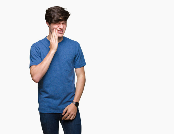 junger gutaussehender Mann, der ein blaues T-Shirt über isoliertem Hintergrund trägt und den Mund mit schmerzhaftem Gesichtsausdruck berührt, weil Zahnschmerzen oder Zahnkrankheiten an den Zähnen auftreten. Zahnarztkonzept. - Foto, Bild