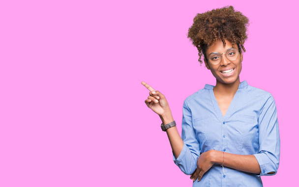Красивая молодая африканская деловая женщина на изолированном фоне с широкой улыбкой на лице, указывая рукой и пальцем в сторону, глядя в камеру
. - Фото, изображение