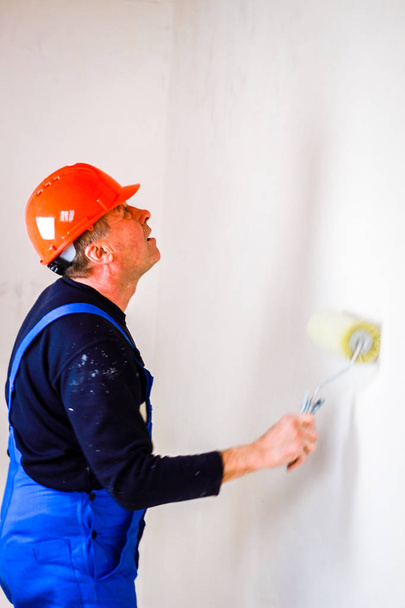 ein Bauarbeiter in einem orangefarbenen Baubecher in der Hand mit einem Spucken - Foto, Bild