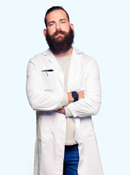 Young blond scientist man wearing white coat skeptic and nervous, disapproving expression on face with crossed arms. Negative person. - Foto, immagini