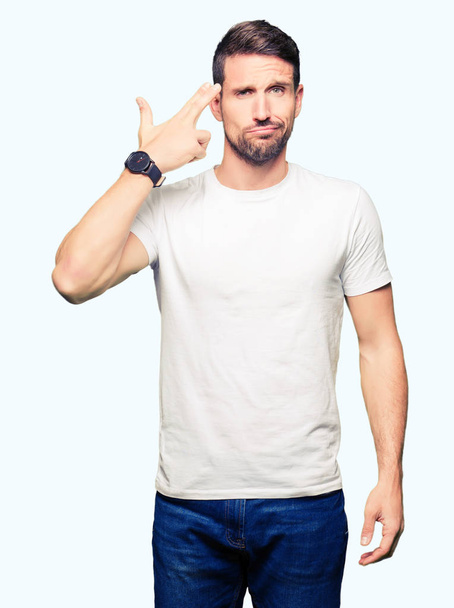 Pohledný muž nosí ležérní bílé tričko střílečky a usmrcují ukazující ruku a prsty do čela, sebevraždou. - Fotografie, Obrázek