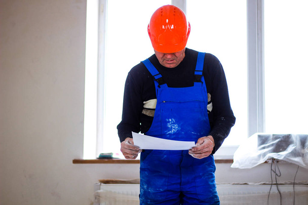 Um construtor em um coletor de construção laranja em suas mãos com o dr
 - Foto, Imagem
