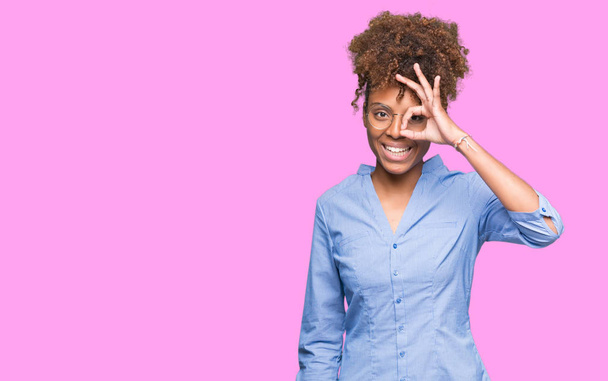 Beautiful young african american business woman over isolated background doing ok gesture with hand smiling, eye looking through fingers with happy face. - Foto, imagen