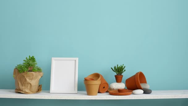 Moderne kamer decoratie met Picture Frame mockup. Witte plank tegen pastel Turquoise muur met aardewerk en succulente installatie. Hand drenken potplant succulente installatie. - Video
