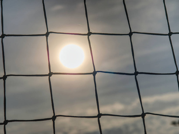 Puerta de fútbol con puesta de sol. Detalle de la red de tenis en pista
 - Foto, imagen