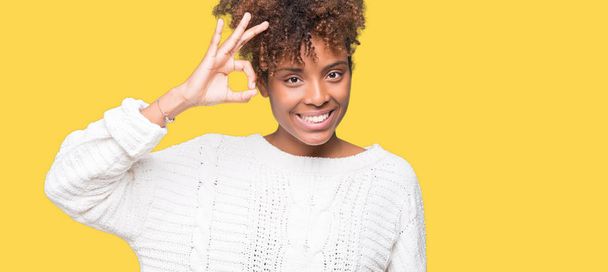 Belle jeune femme afro-américaine portant un pull d'hiver sur fond isolé souriant positif faisant signe ok avec la main et les doigts. Expression réussie
. - Photo, image
