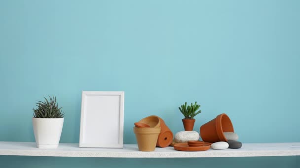 Modern room decoration with picture frame mockup. White shelf against pastel turquoise wall with pottery and succulent plant. Hand watering potted succulent plant. - Footage, Video