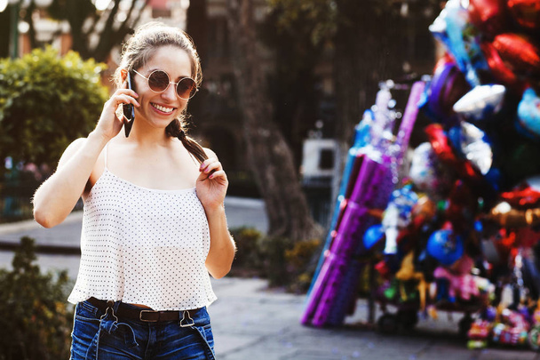 Laughing latin girl portrait, female teenager at smart phone outdoor in a colonial city in Mexico - Zdjęcie, obraz