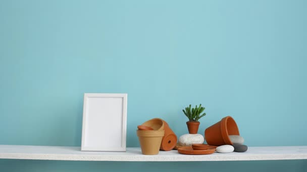 Modern room decoration with picture frame mockup. White shelf against pastel turquoise wall with pottery and succulent plant. Hand putting down potted snake plant. - Footage, Video