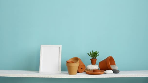 図フレームモックアップ付きのモダンな客室の装飾。陶器とジューシーな植物とパステルターコイズの壁に対する白い棚。鉢植えのクモの植物を置く手. - 映像、動画