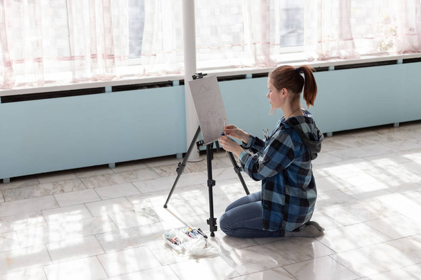 La artista está sentada en el suelo de baldosas de mármol. Mujer en el proceso de dibujo pinturas al óleo
. - Foto, Imagen