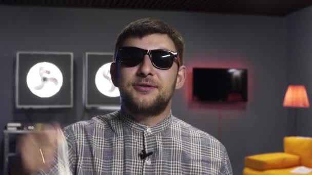 Joven vlogger masculino habla activamente y balancea bolsa blanca en la cámara con sonrisa
 - Metraje, vídeo