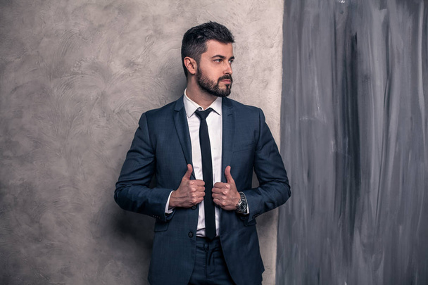 Bonito empresário bonito está de pé em seu escritório e pensando. Vestindo terno e gravata
 - Foto, Imagem
