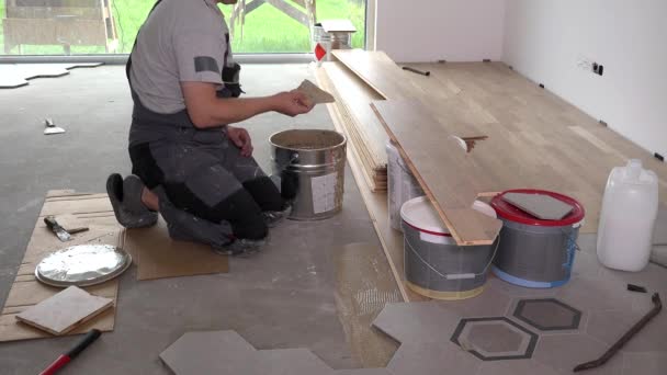 Człowiek stosuje klej kleju na podłodze do układania deski parkietu - Materiał filmowy, wideo