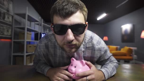 Bearded knappe man spreekt en kijkt naar camera Holding Piggy Bank in handen - Video