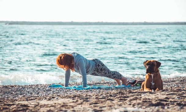 girl doing yoga and stretching on the beach with her dog - Photo, Image