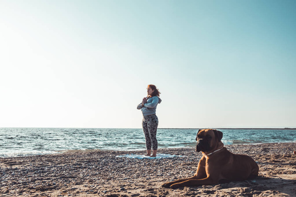 girl doing yoga and stretching on the beach with her dog - Valokuva, kuva