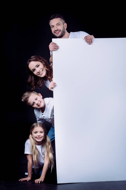 Happy family holding blank white card and looking at camera on black - Foto, immagini