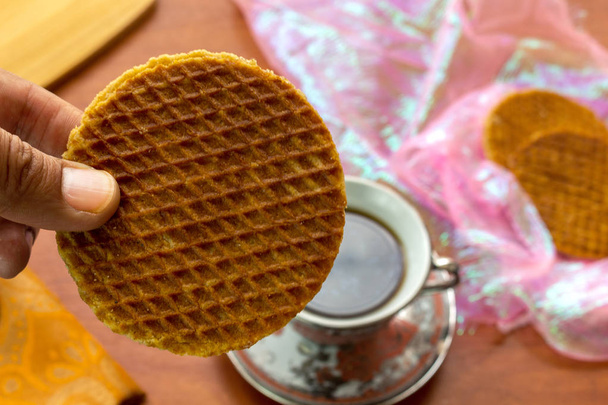 Close-up of stroopwafel with a hand bringing it to a cup of coffee - Foto, imagen