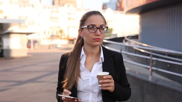 Jovem mulher de negócios com café bebida smartphone na rua da cidade. Disparo firme
 - Filmagem, Vídeo